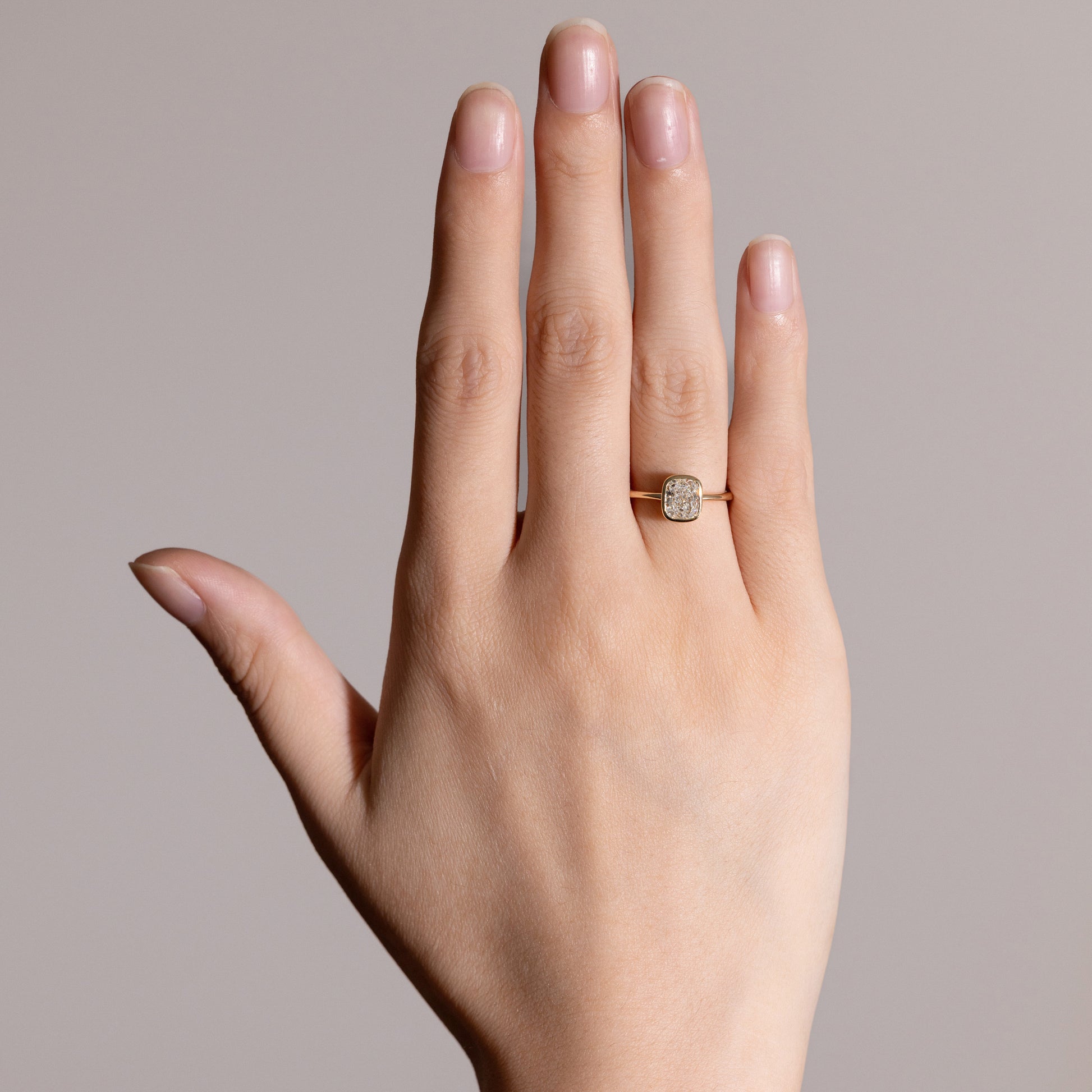 Close-up detail of Cushion cut lab-grown diamond in smooth bezel setting on model’s finger