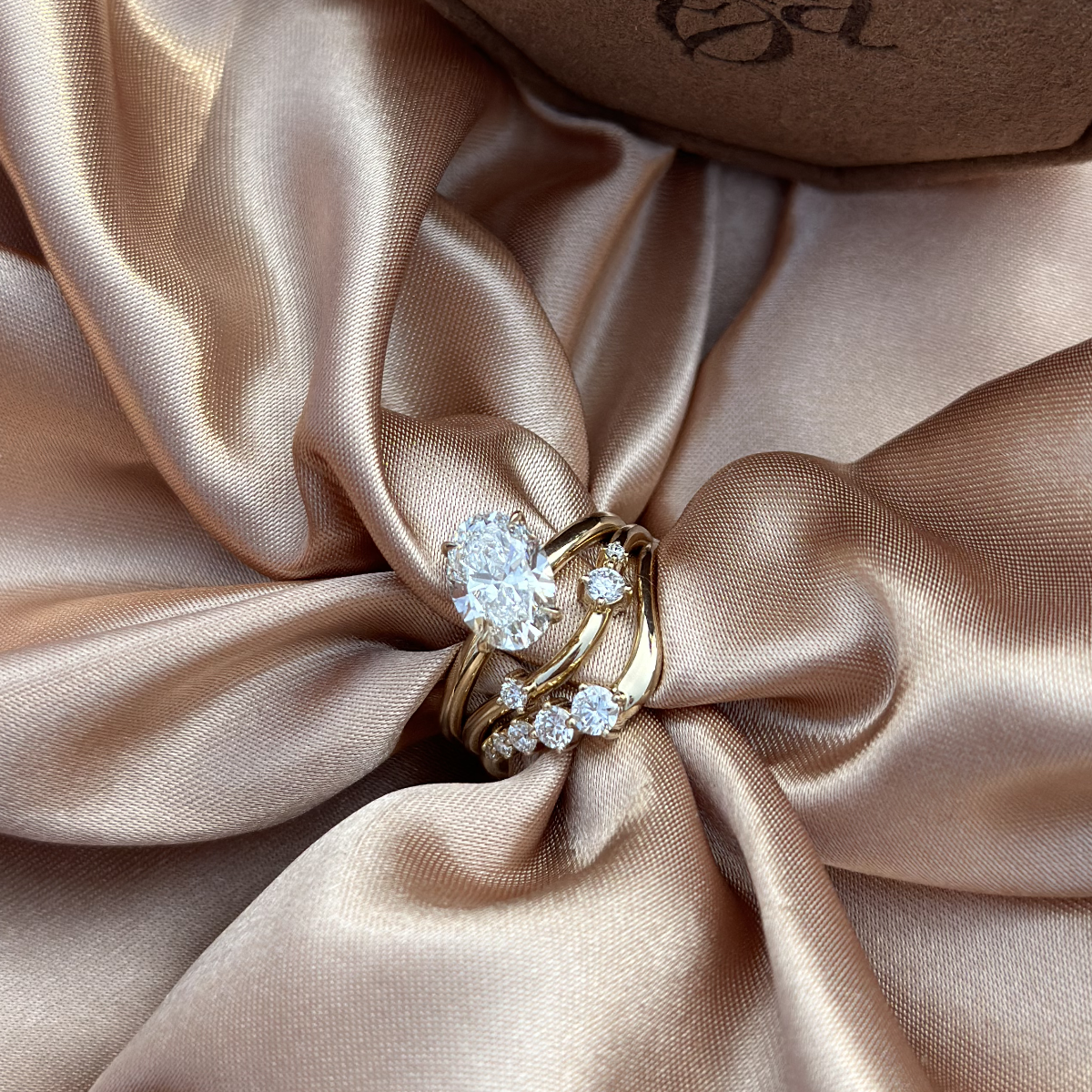 Elegant tilted oval diamond ring displayed on champagne silk fabric with matching bands