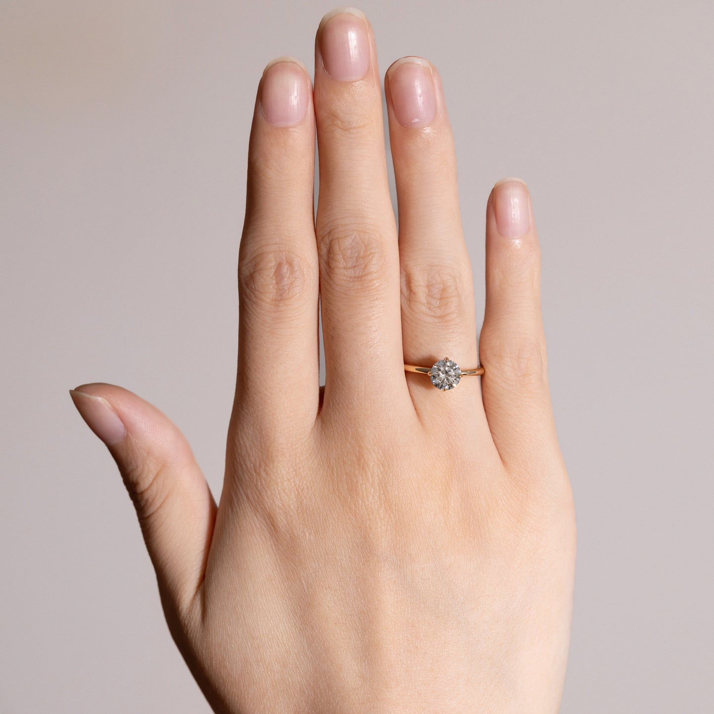 Hand raised to display Layla Round Cut diamond solitaire engagement ring in soft daylight