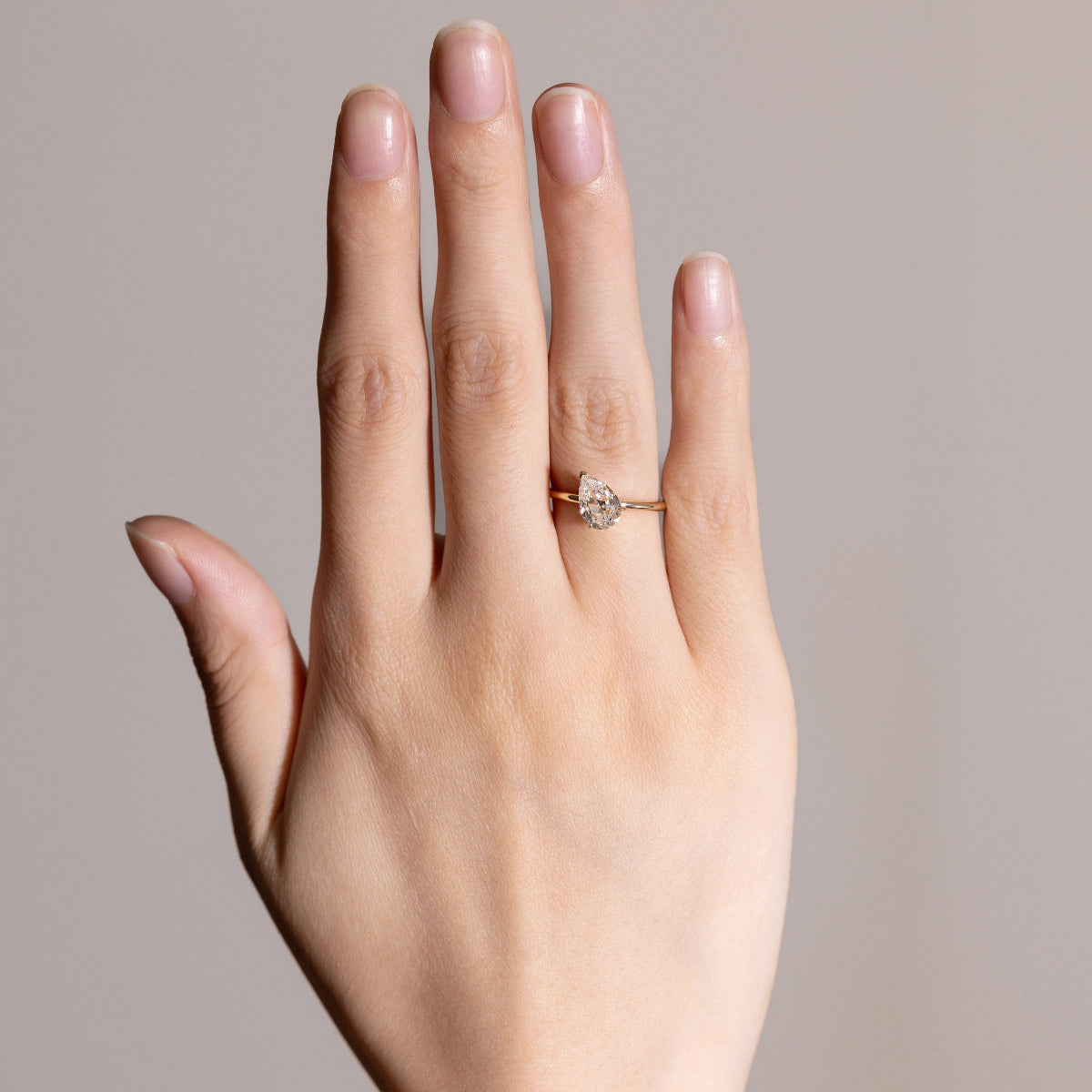 Model hand wearing Tilted Pear cut diamond solitaire ring in minimalist style