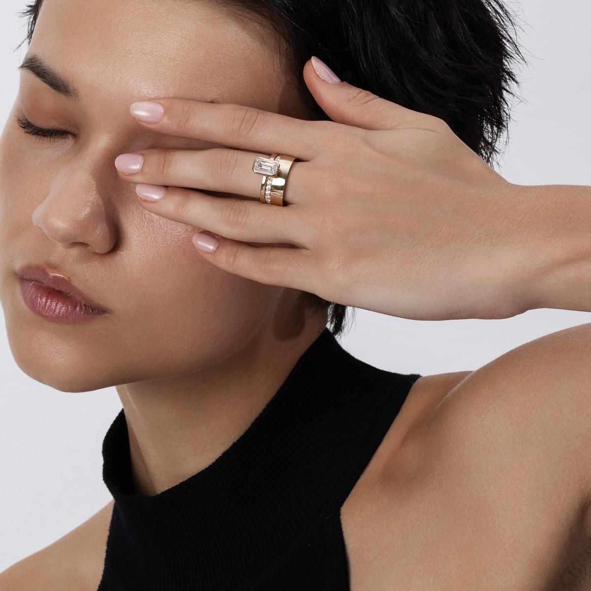 Model styling bezel emerald cut diamond engagement ring with stacking wide gold bands for a bold layered look