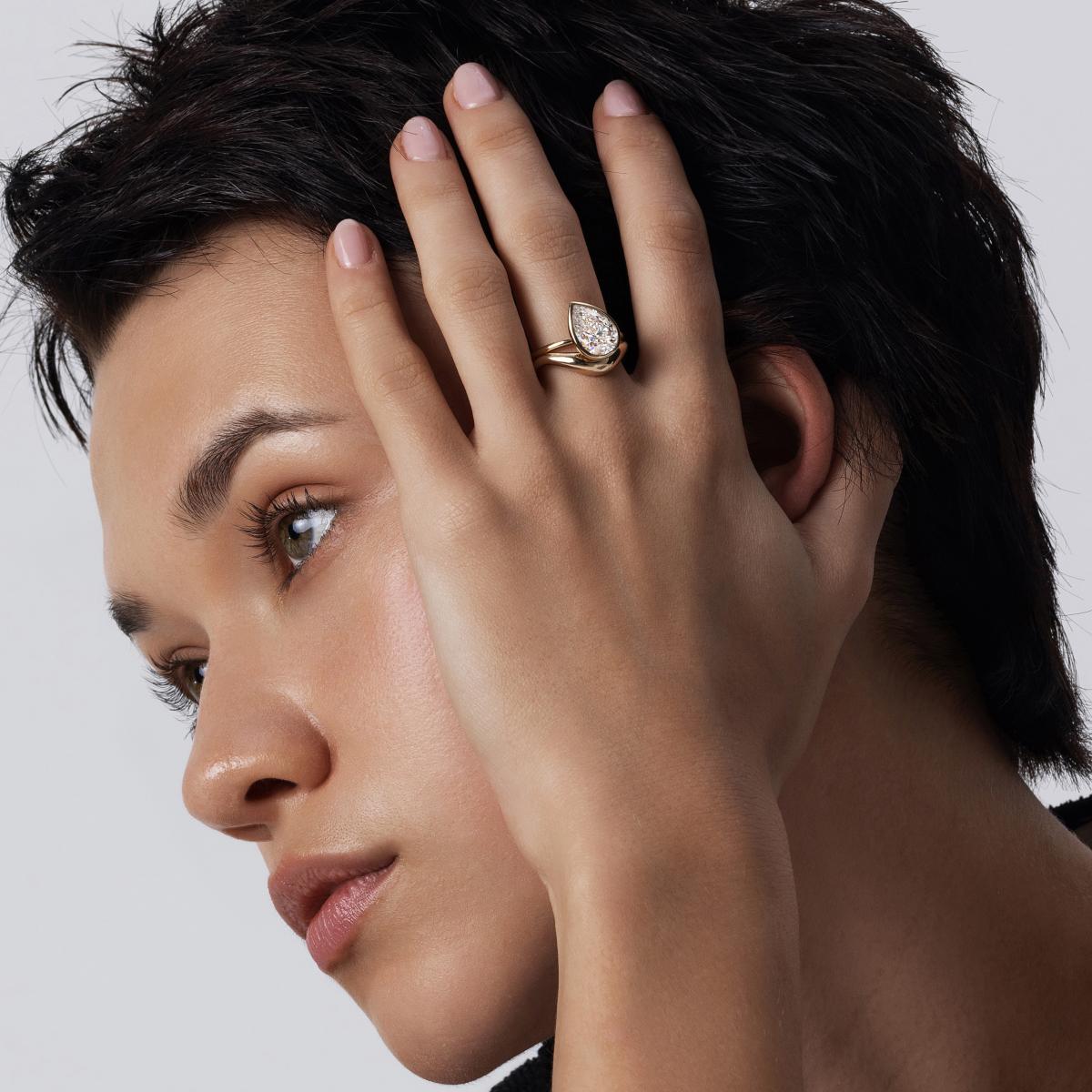 Model wearing Tilted Pear-cut bezel diamond ring stacked with a curved band