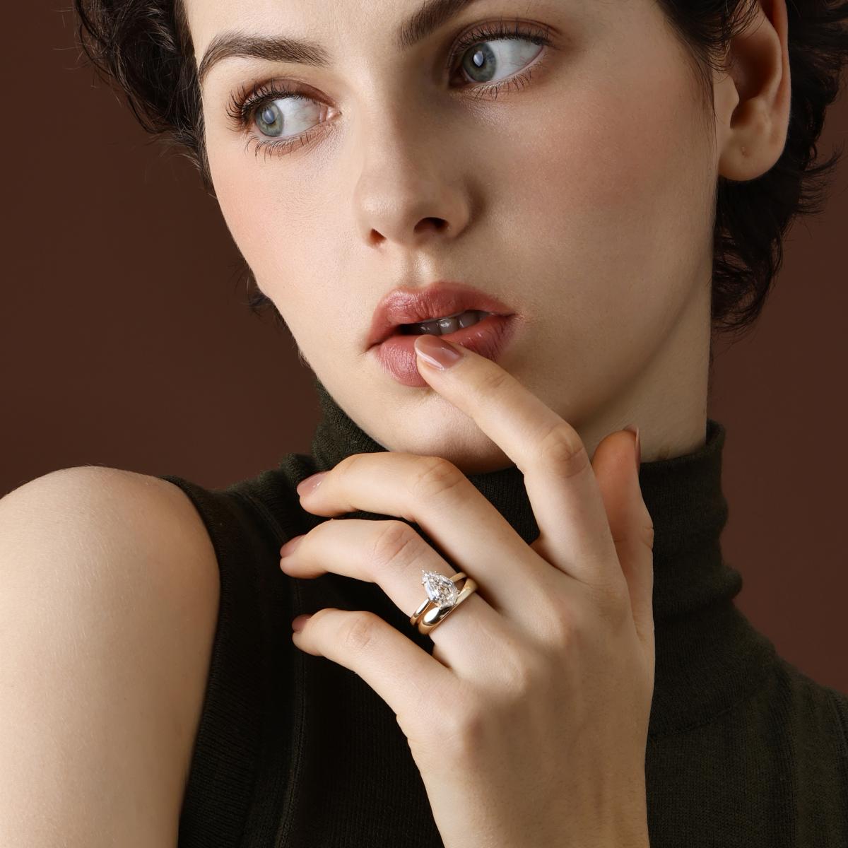 Model wearing step cut pear lab grown diamond engagement ring in a stacked ring look