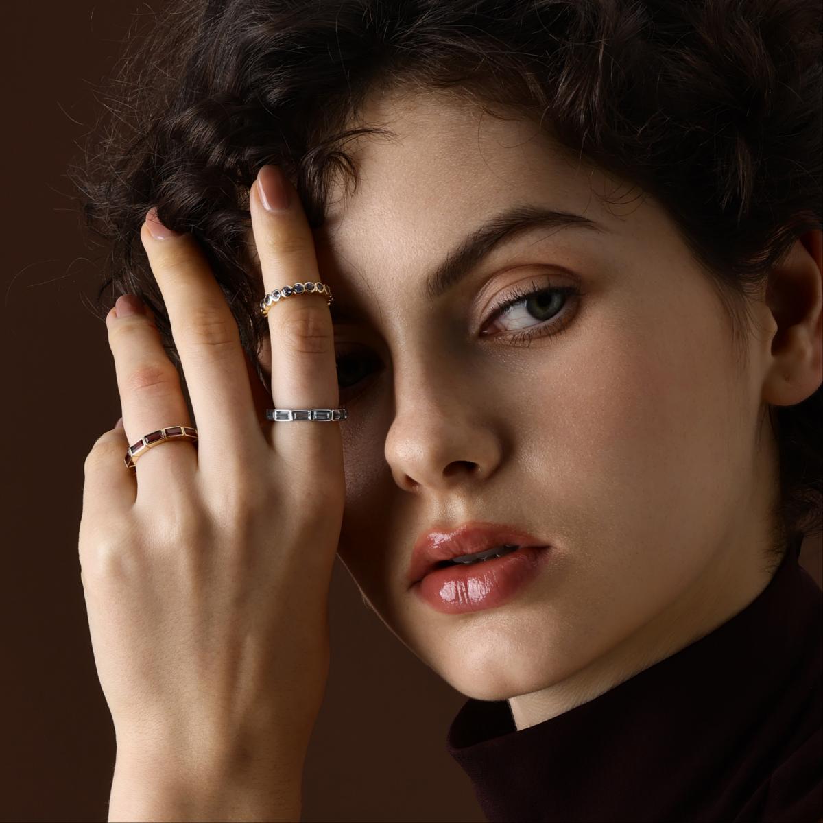 Model wearing a baguette cut topaz eternity band in platinum styled with other rings