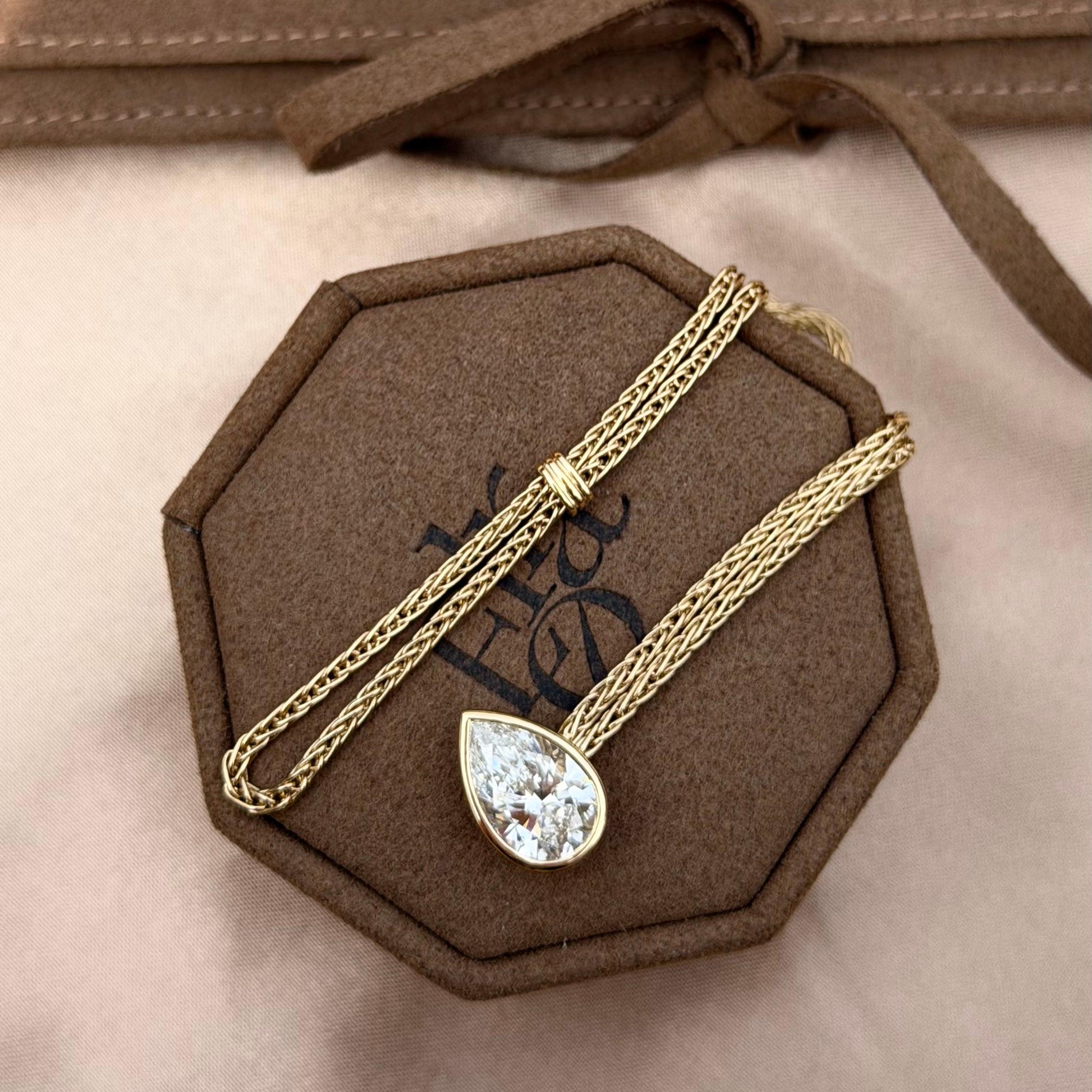 Faith-Pear Cut Lab Grown Diamond Bracelet displayed on a brown octagonal box, featuring a pear-cut diamond and gold chain.