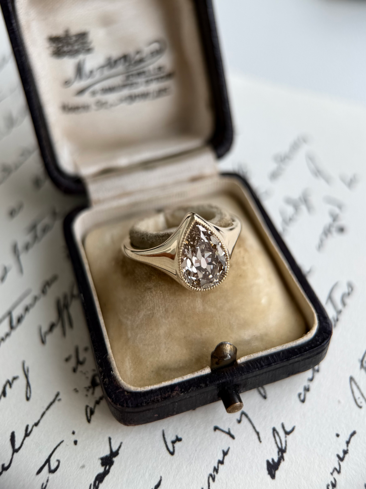Eddy-Champagne Old Mine Pear Lab Grown Diamond Ring displayed in a vintage jewelry box on handwritten notes.