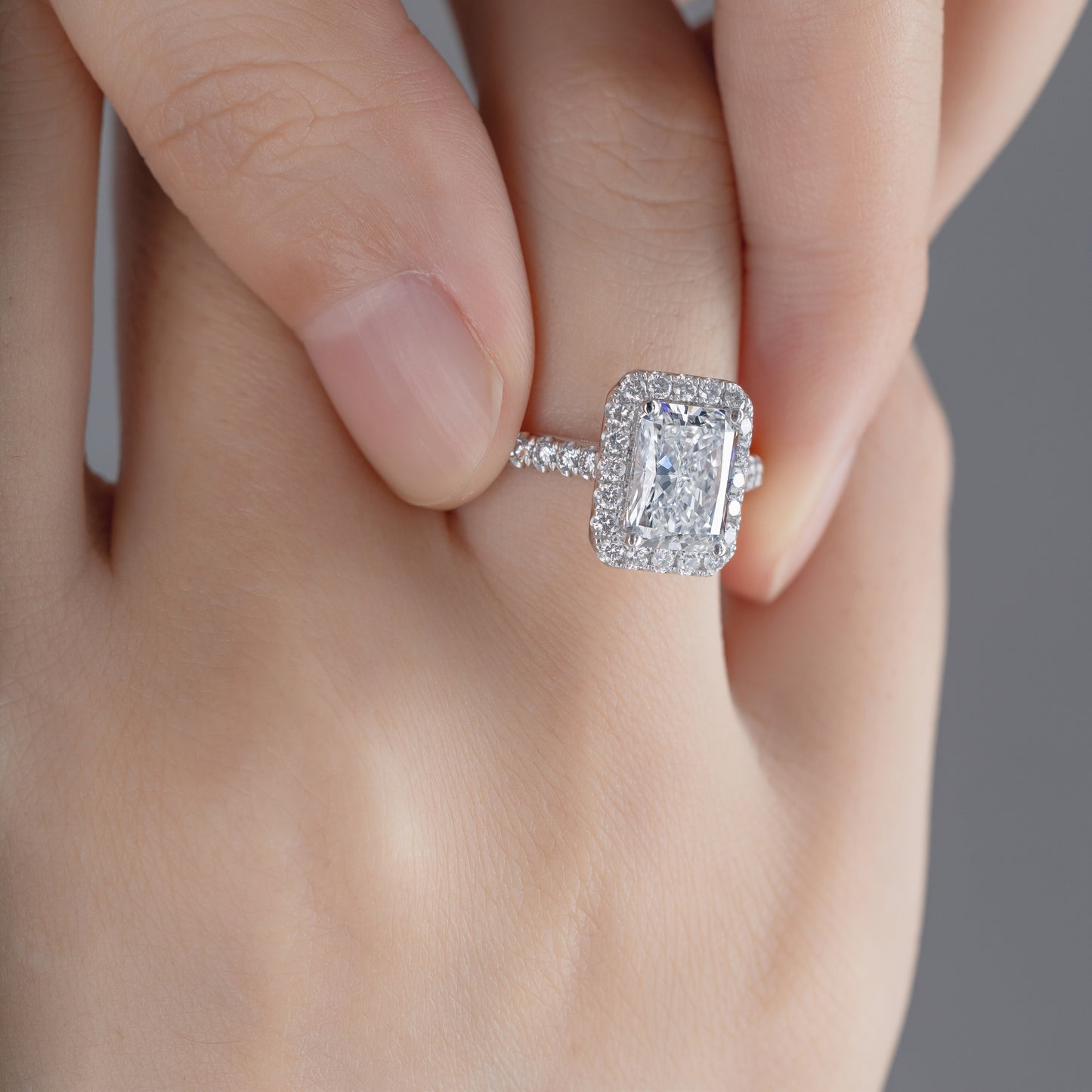 Close-up of Radiant cut Lab Grown diamond in a pave setting Halo Engagement Ring on model’s finger