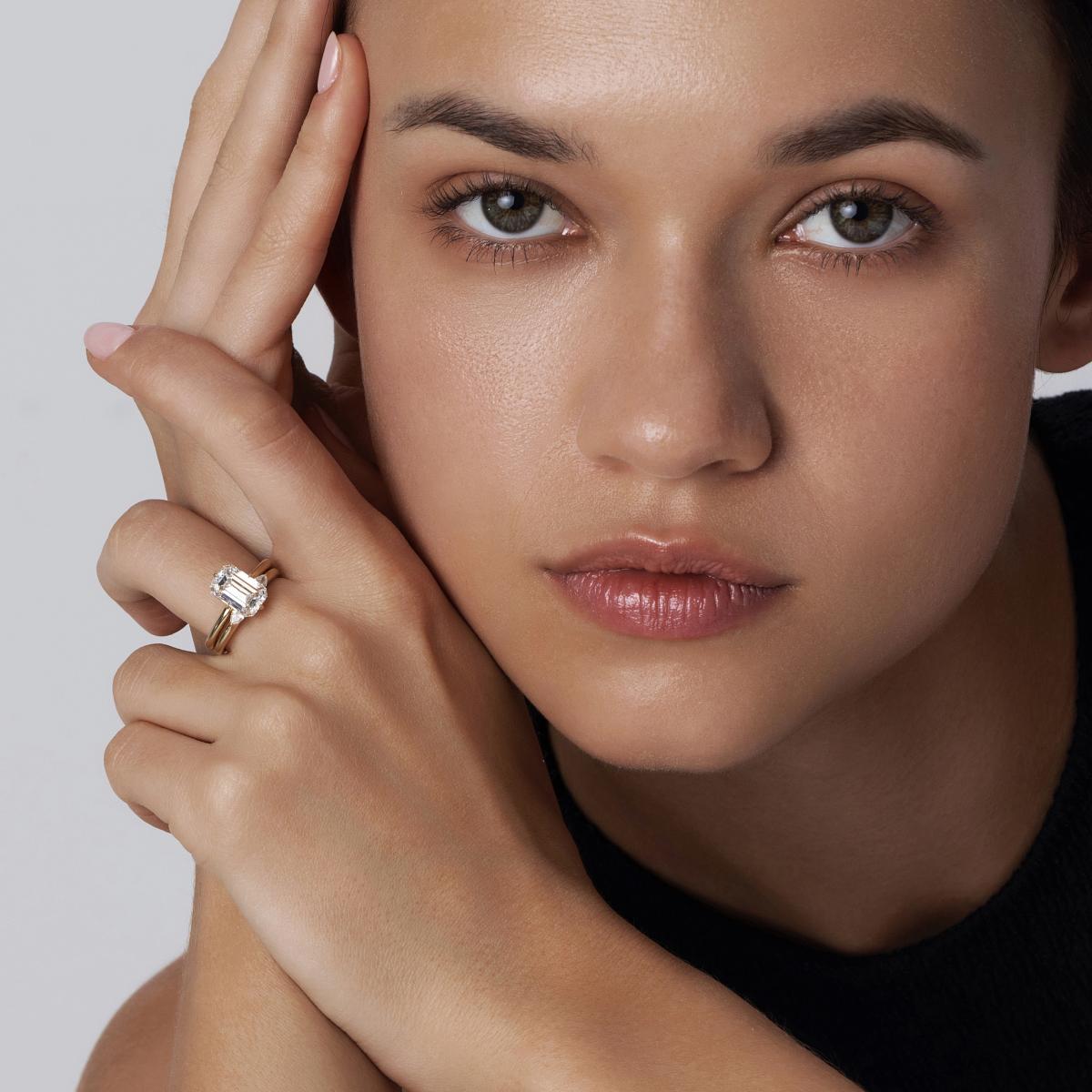 Engagement ring of Emerald cut diamond and matching open band stacked on model’s hand