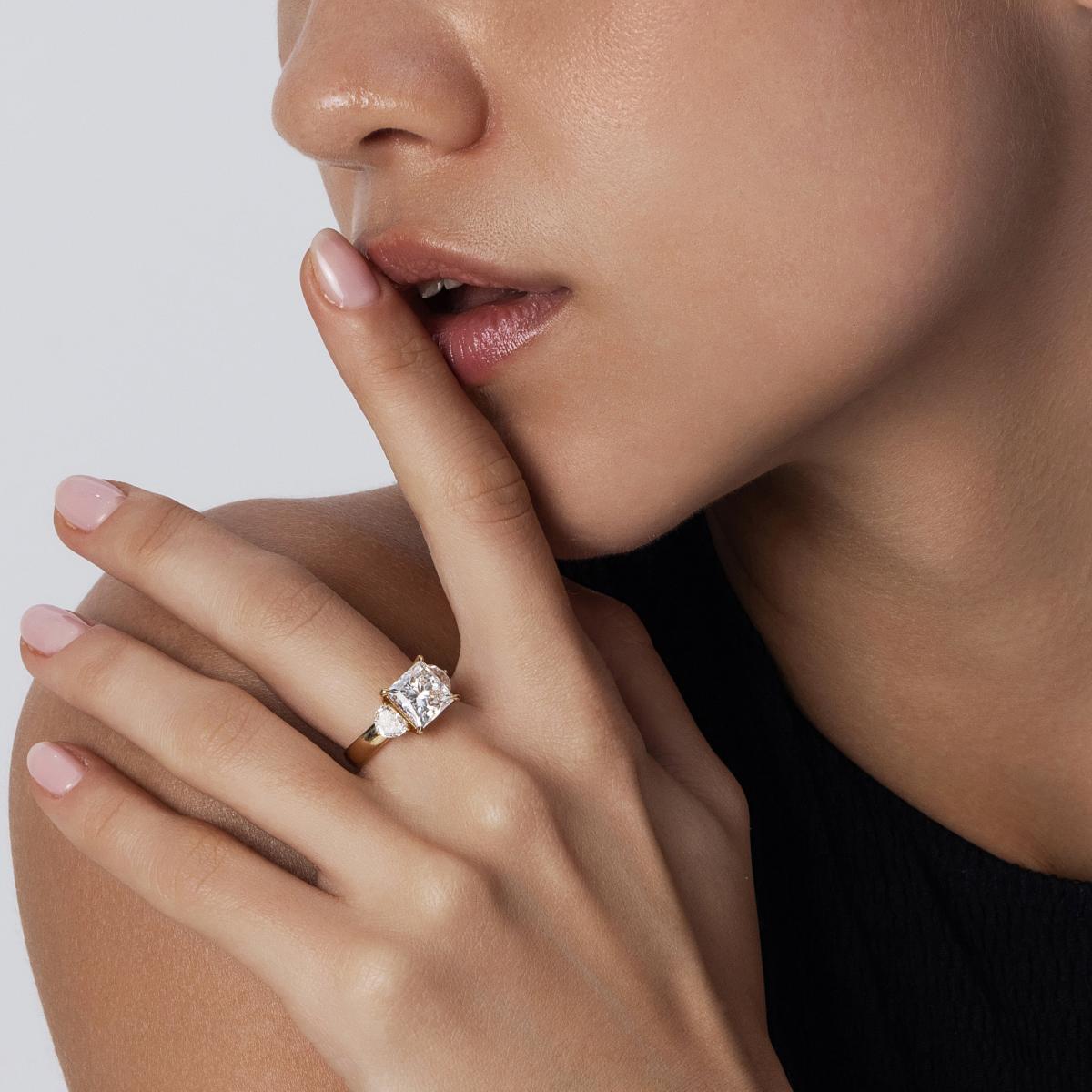Three-stone Princess Cut diamond ring styled on model’s hand in yellow gold