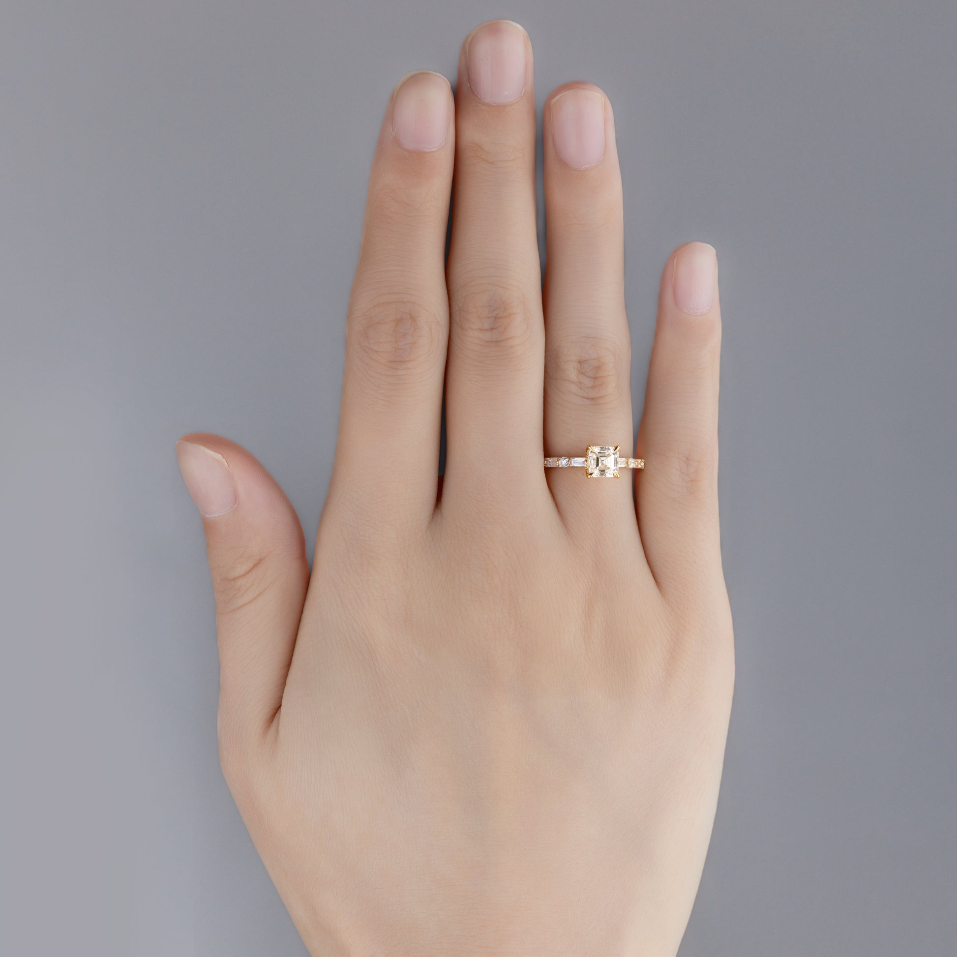 Top view of hand wearing Asscher cut lab-grown diamond pavé ring with Side stones in 14K gold