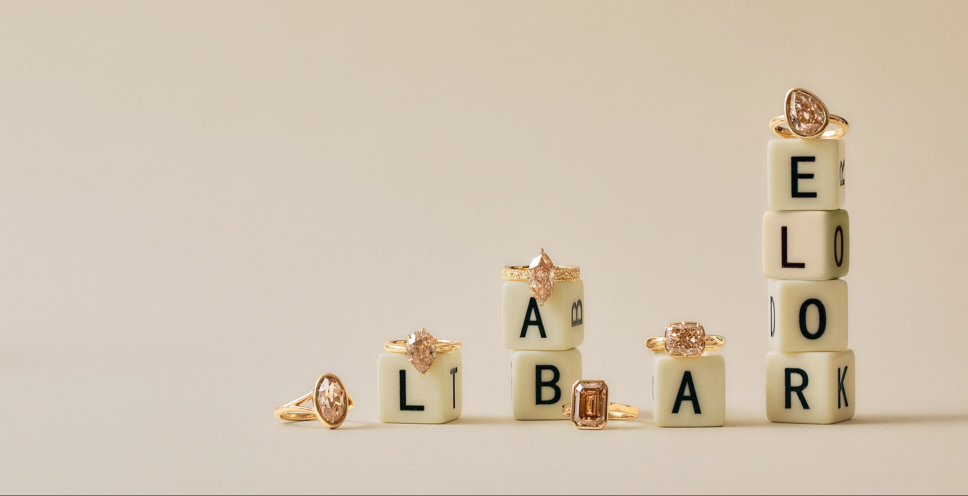 Five gold rings with clear gemstones are arranged on top of cream letter blocks spelling out 'LOOK BACK' on a warm beige background.